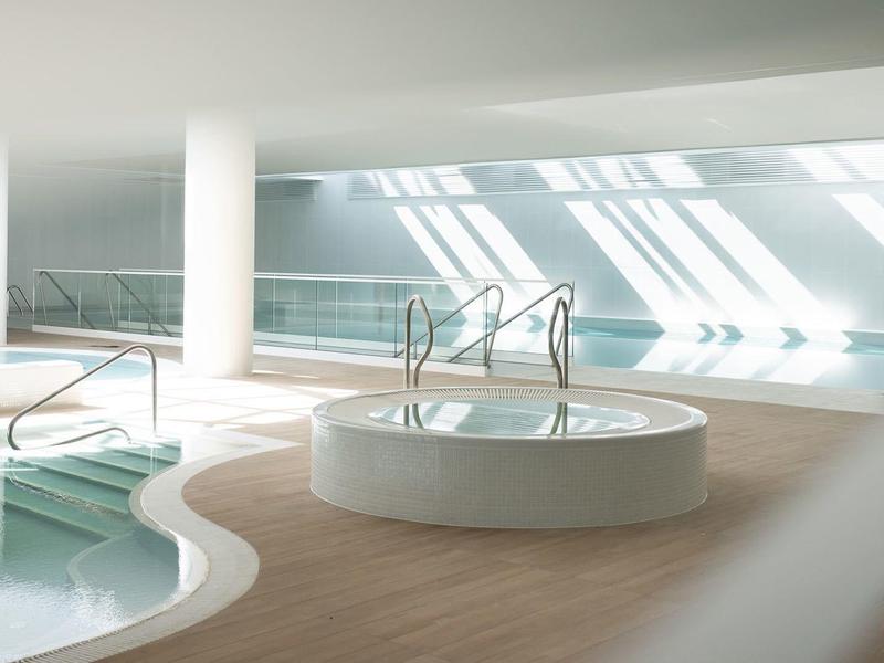 Moderner Innenpoolbereich mit hellem Holzfußboden, Säulen und großen Fenstern für Tageslicht.