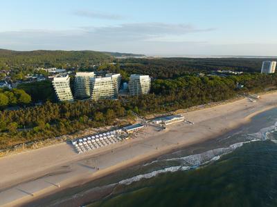 Blick auf einen Sandstrand mit Sonnenliegen, dahinter Hotels und bewaldete Hügel.