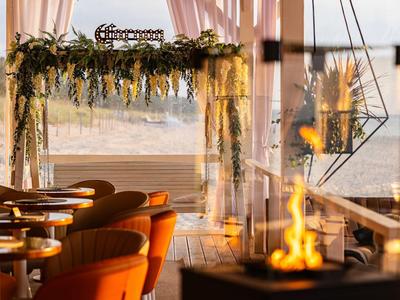 Restaurant mit orangefarbenen Stühlen, hängender Dekoration und offenem Blick aufs Meer bei Sonnenuntergang.