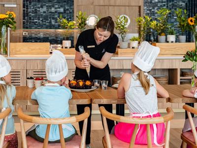 Kinderen met koksmutsen zitten aan een tafel terwijl een chef-kok het koken laat zien.