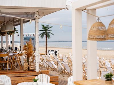Strandterras met houten stoelen en palmbomen met uitzicht op rustige zee.