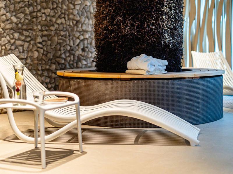 Moderne lounge met witte stoel en tafel naast ronde houten tafel en stenen muur.