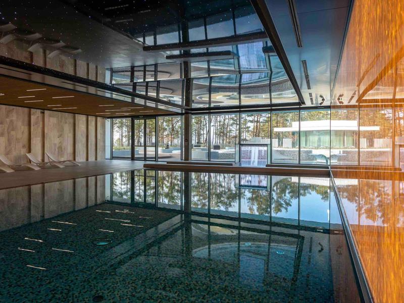 Binnenzwembad met glazen wanden met uitzicht op bomen en gebouwen op de achtergrond.