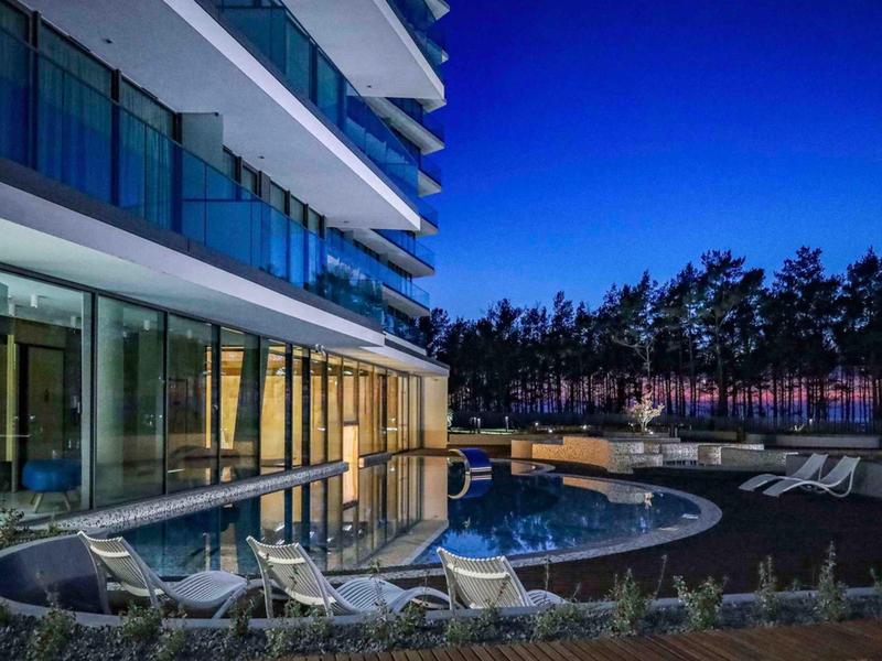 Moderne hotelbuitenruimte met zwembad, ligstoelen en glazen gevel in de avond.