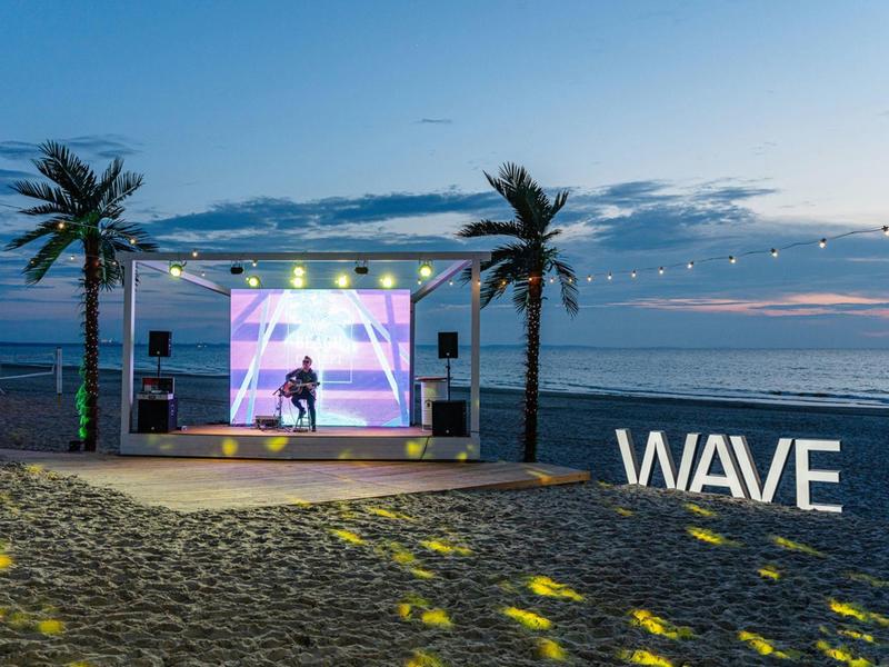 Strandpodium met verlichting en WAVE-bord bij zonsondergang aan zee