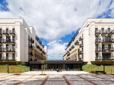 Zwei moderne Wohngebäude mit Balkonen und einem Verbindungsgang bei bewölktem Himmel.