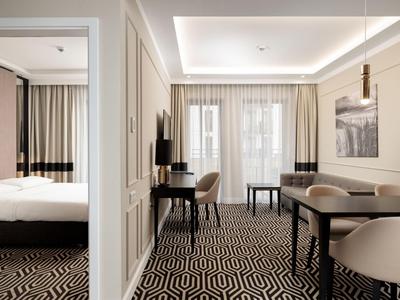 Modern eingerichtetes Hotelzimmer mit Schreibtisch, Stuhl, Bett und gemustertem Teppichboden.