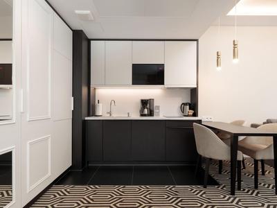 Moderne Küchenzeile mit schwarzen Unterschränken, weißen Oberschränken und Essbereich mit zwei Stühlen.