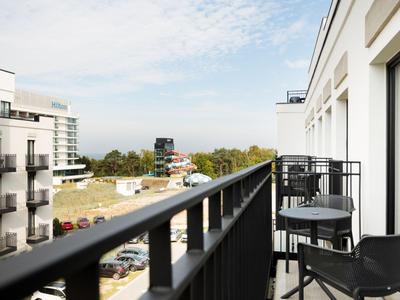 Balkon mit Stühlen und Tisch, Blick auf Wohngebäude und Straße bei klarem Himmel.