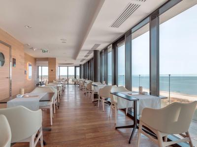 Modernes Restaurant mit weißen Stühlen und großen Fenstern mit Meerblick.