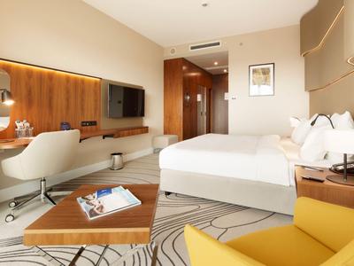 Modern eingerichtetes Hotelzimmer mit Doppelbett, Schreibtisch, Fernseher und gemütlichem Sessel.