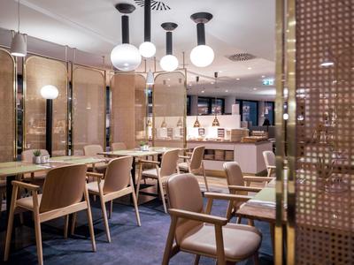 Modern eingerichteter Speiseraum mit Tischen, Stühlen und runden Deckenleuchten.