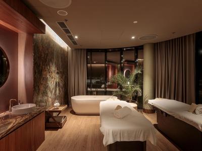 Eleganter Spa-Raum mit zwei Massageliegen, freistehender Badewanne und gedämpfter Beleuchtung.