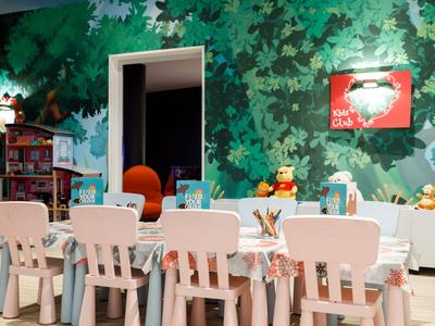 Gemütlicher Kinderraum mit kleinen Tischen, Stühlen und bunter Wanddekoration im Hotel.