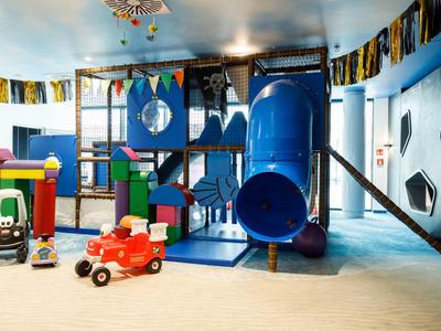 Bunter Indoor-Spielplatz mit Rutsche, Klettergerüst und Spielzeugautos in einem hellen Raum.