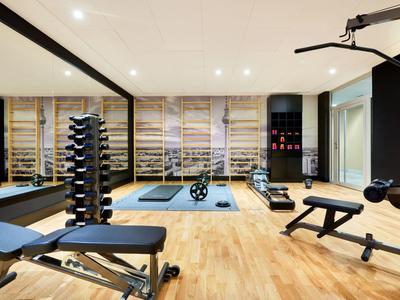 Moderner Fitnessraum mit Hanteln, Trainingsbänken und Weinkeller im Hintergrund.