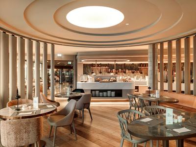 Modernes, elegantes Restaurant mit runden Tischen und Stühlen, beleuchtet durch eine runde Deckenöffnung.