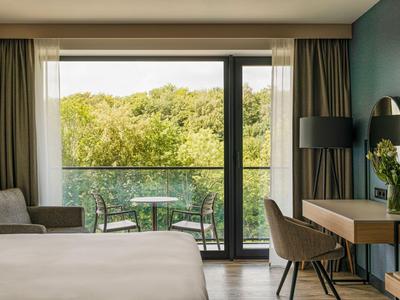 Gemütliches Hotelzimmer mit Balkon und Blick auf grüne Bäume.