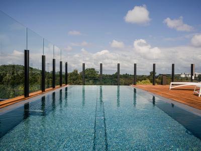 Moderner Pool mit Glasgeländer und Liegestühlen, umgeben von grüner Landschaft und blauem Himmel.