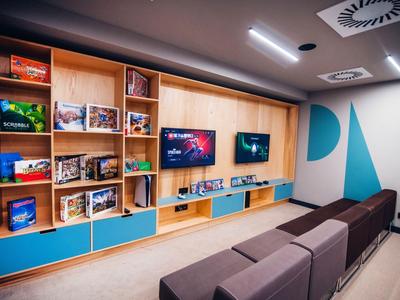 Moderner Aufenthaltsraum mit ergonomischen Sitzbänken, Holzregalen und Wandbildschirmen.