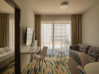 Camera d'hotel moderna con divano, TV e balcone con vista sugli edifici.