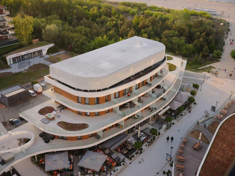 Terrazze moderne curve dell'hotel con aree esterne affacciate su una spiaggia boschiva.