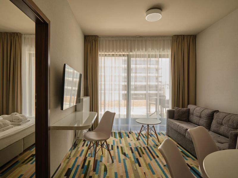 Camera d'hotel moderna con divano, TV e balcone con vista sugli edifici.