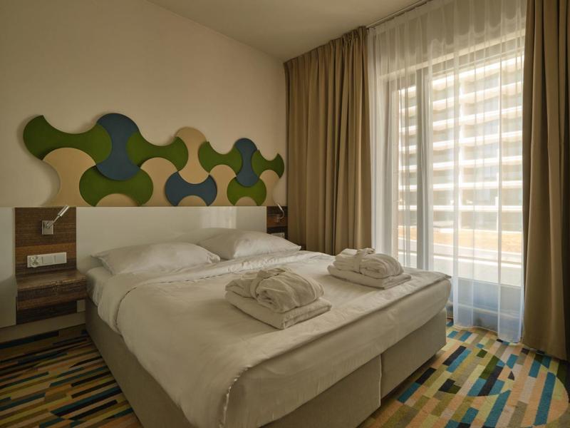 Camera d'hotel moderna con letto matrimoniale, tappeto colorato e decorazione geometrica sulla parete vicino a finestra con tende.