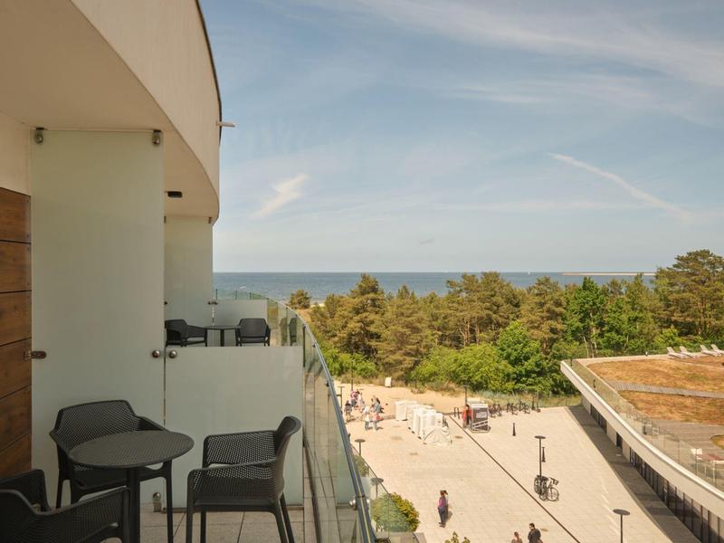 Balcone con sedie che domina la foresta, la spiaggia e il mare sotto un cielo azzurro.