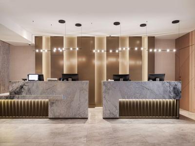 Moderner Hotel-Empfang mit zwei grauen Marmorrezeptionen und goldenen Akzenten.