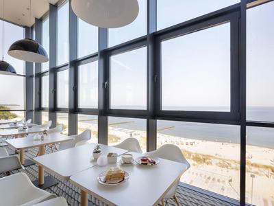 Modernes Café mit großen Fenstern und Blick auf Strand und Meer.