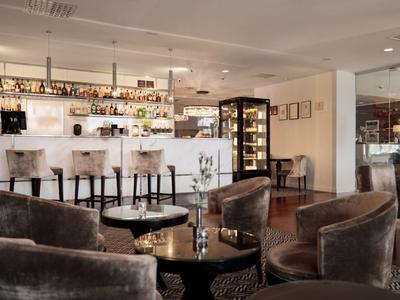 Moderne Hotelbar mit weißer Theke, Barhockern und gemütlichen Samtsesseln.