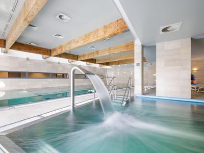 Modernes Hallenbad mit Wasserfall und Holzdeckenbalken in einem Hotel.