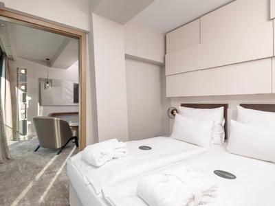 Modernes Hotelzimmer mit Doppelbett, weißen Bettwäsche und angrenzendem Sitzbereich mit Stuhl.