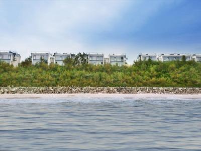 Diverse case a schiera dietro cespugli vicino alla spiaggia sotto un cielo azzurro