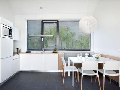 Moderne weiße Küche mit Essbereich, großem Fenster und minimalistischer Einrichtung.