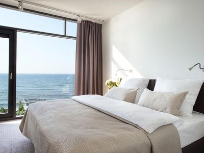 Modernes Hotelzimmer mit großem Bett und Blick auf das Meer durch große Fenster.