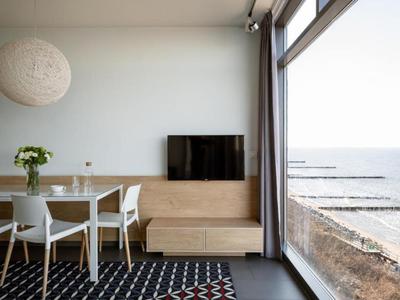 Moderner Essbereich mit Fernseher und Blick auf das Meer durch große Fenster.