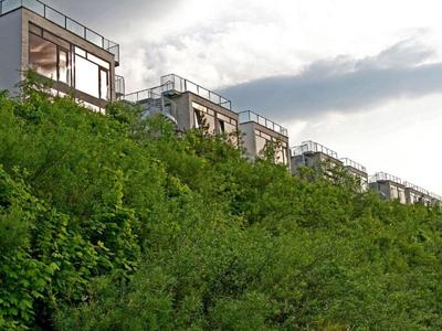 Moderne Häuser mit großen Fenstern und Dachterrassen auf einem bewaldeten Hügel.