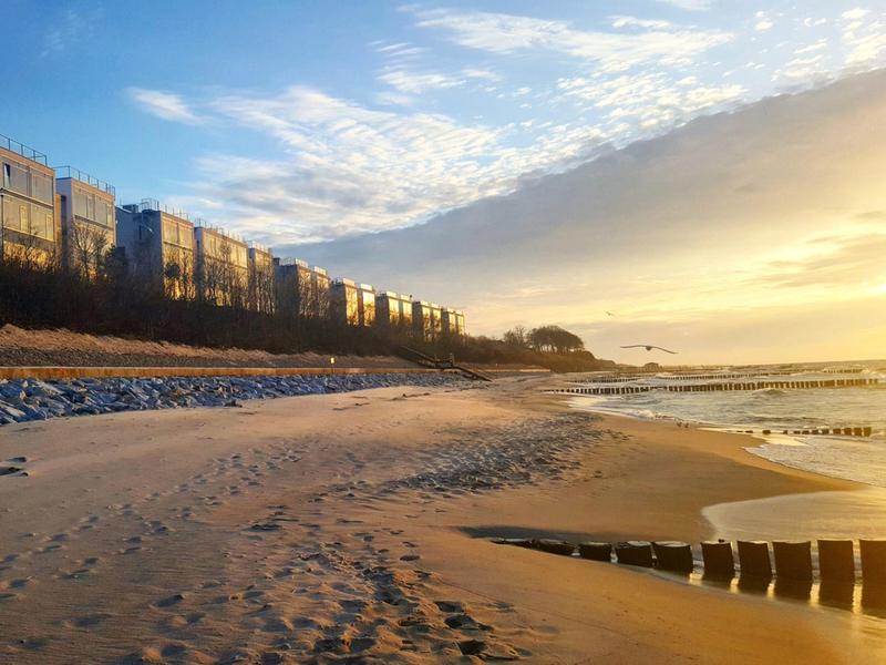 Plage au coucher du soleil, sable, brise-lames et bâtiments en arrière-plan.