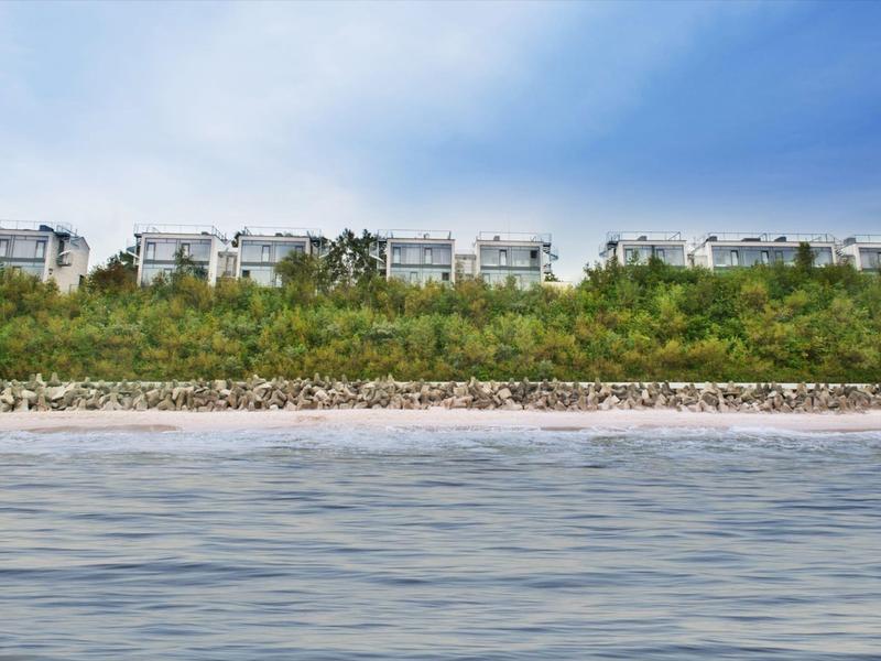 Plusieurs maisons en rangée derrière des buissons près de la plage sous un ciel bleu