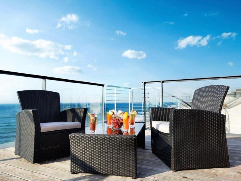 Terrasse avec sièges et boissons avec vue sur la mer par une journée ensoleillée.