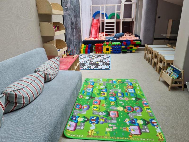 Stanza giochi per bambini con divano, tappeto colorato, giocattoli e piccoli tavoli con sedie.