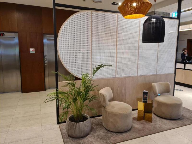 Ingresso moderno di hotel con sedie eleganti, piante e divisorio in legno e tessuto.