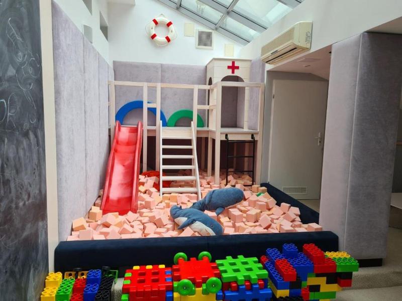 Bambini che giocano al chiuso con struttura per arrampicata, scivolo e blocchi di schiuma.