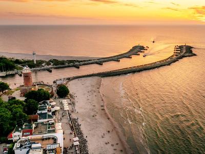 Strand mit Leuchtturm und langer Mole bei Sonnenuntergang über ruhigem Meer