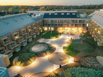 Luxuriöses Hotel mit beleuchtetem Innenhof und begrünter Landschaft bei Dämmerung.