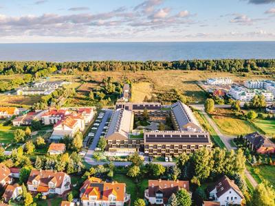 Luftaufnahme einer ruhigen Vorstadtsiedlung mit Grünflächen und weitläufigem Blick aufs Meer.