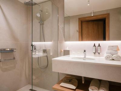 Moderne Hoteldusche mit Glaswand, weißem Waschbecken und Handtüchern auf Holzregal.