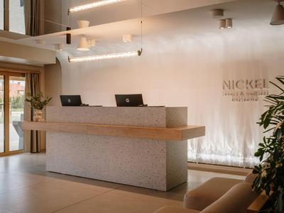 Moderner Hotellobby-Empfang mit minimalistischem Tresen, Laptop-Arbeitsplätzen und natürlichem Licht.